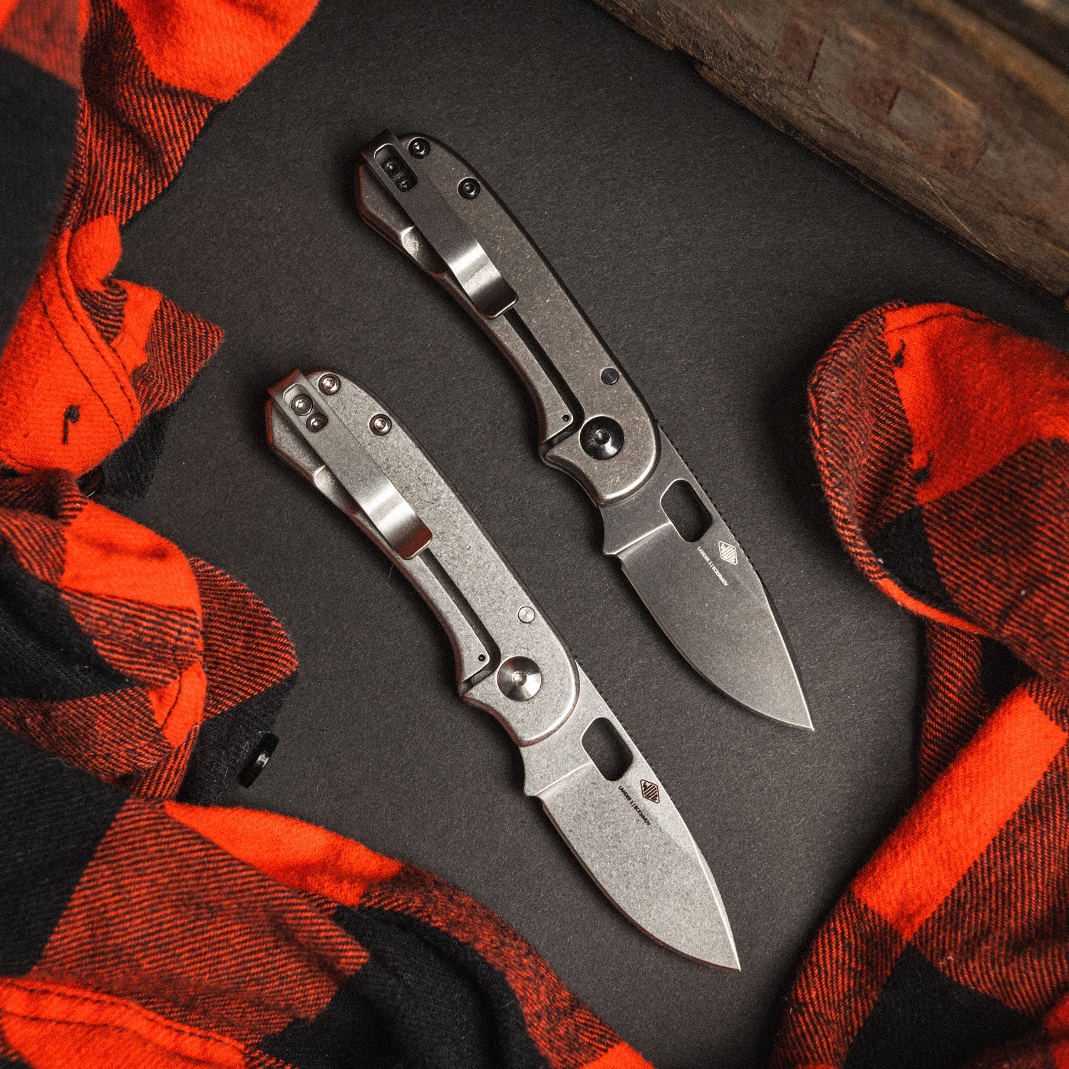 Two Lander 5 folding knives on a dark surface with red and black checkered fabric