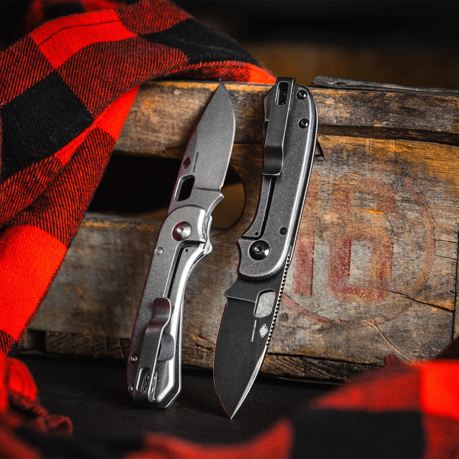 Two folding knives on a wooden surface with a red and black checkered cloth.