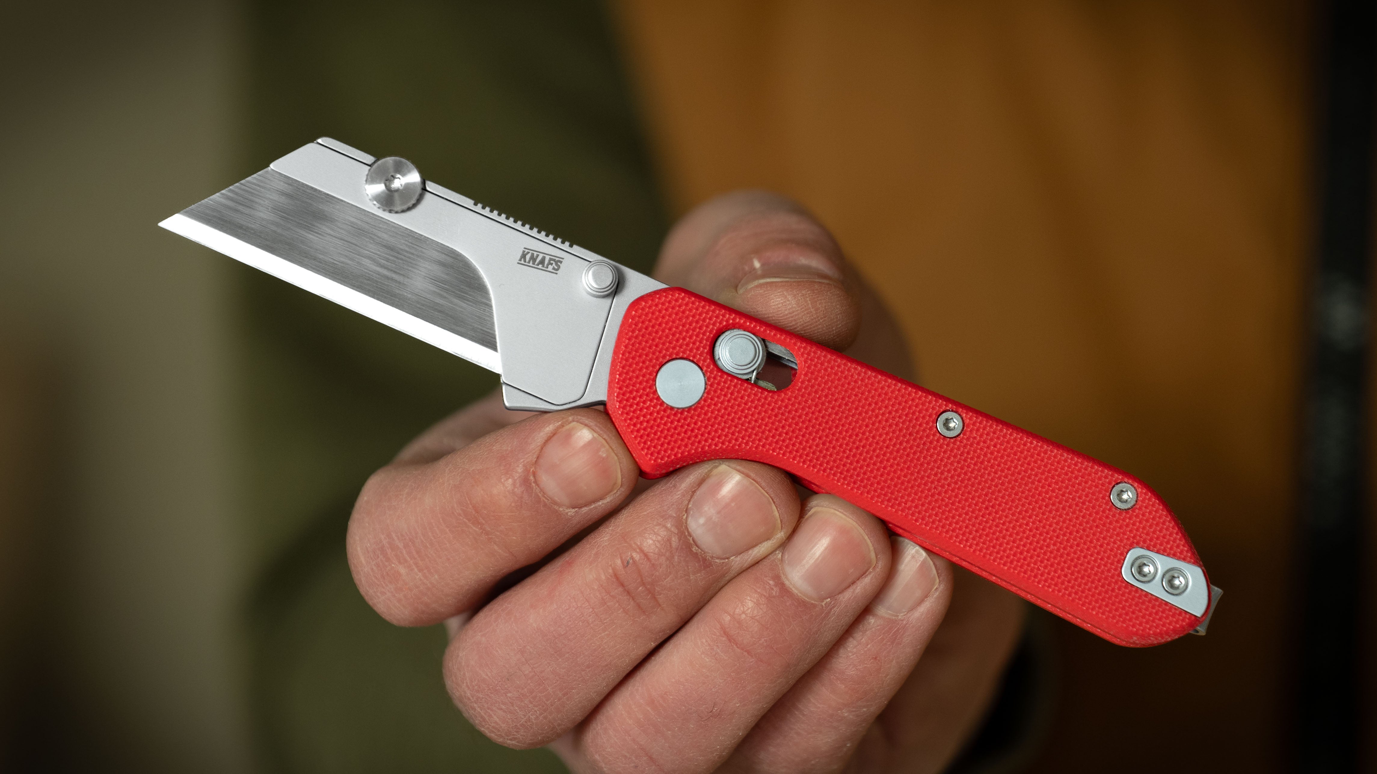 Hand holding open Yuti utility knife with red G10 handle